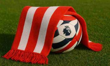 A red and white striped football scarf draped over a modern, unbranded soccer ball on green grass in daylight.